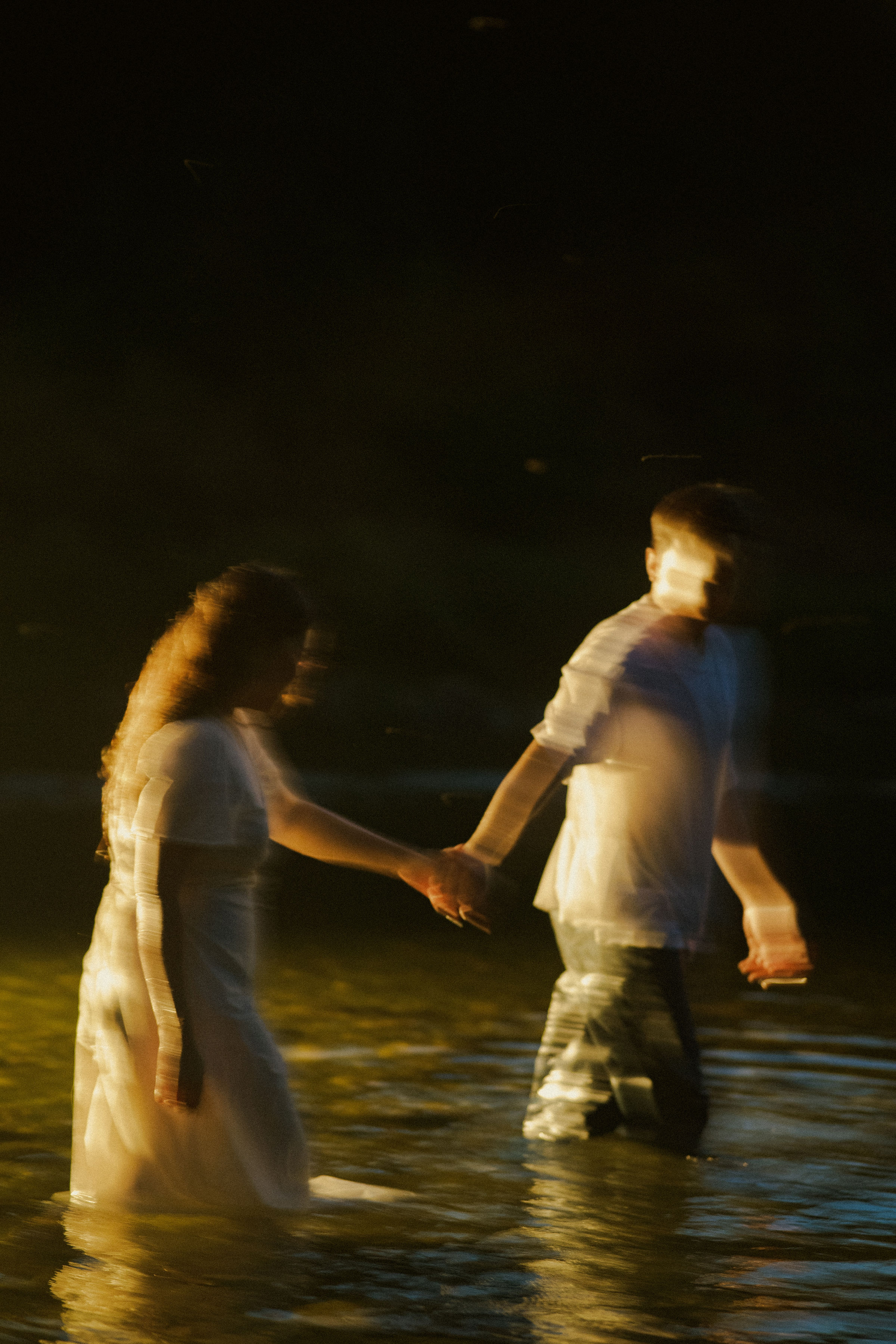 Alexandra and Jerome holding hands in the water at sunset